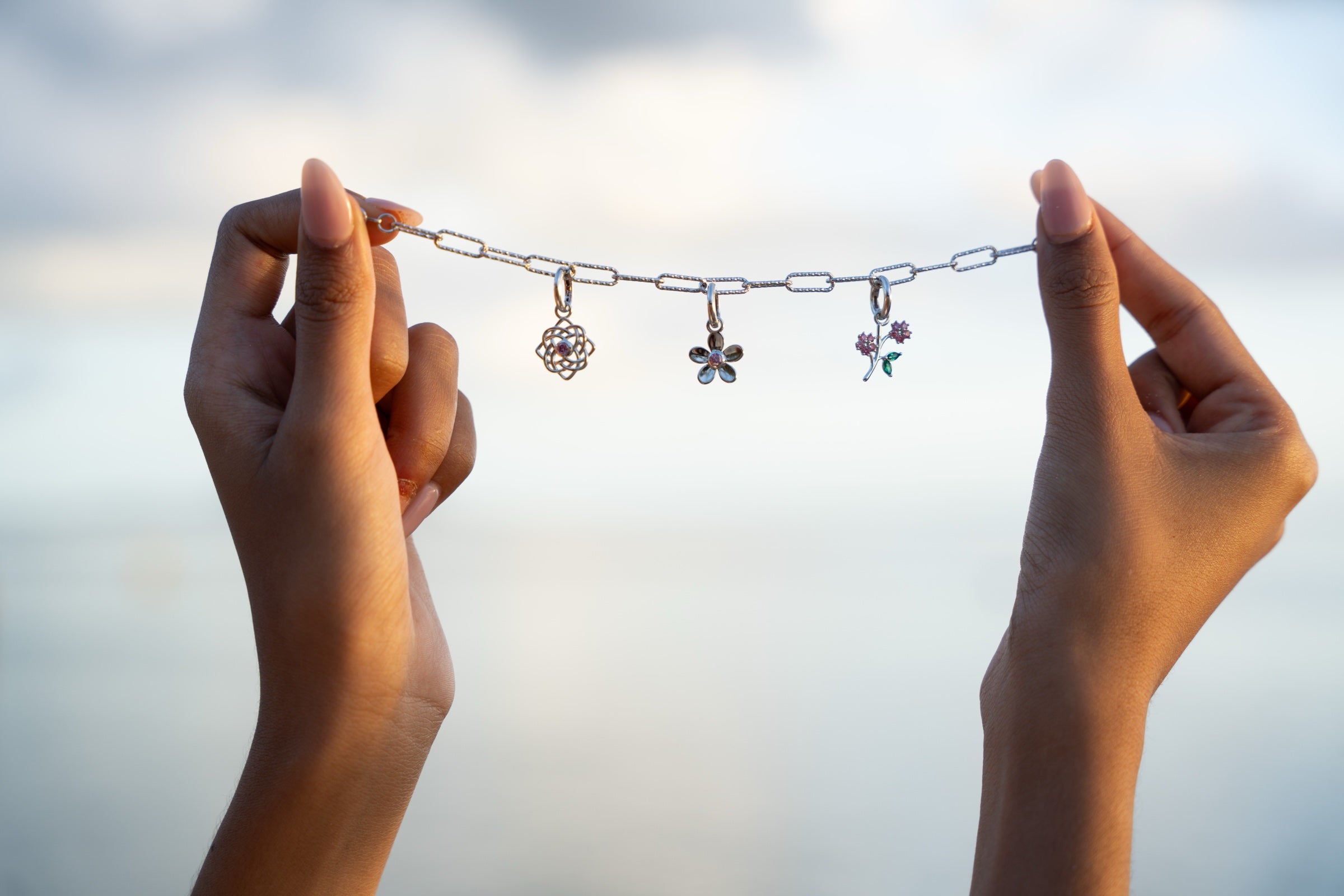 Hands holding a DIVETIA paperclip chain with three meaningful charms